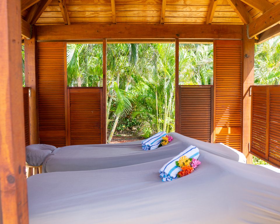 Inside a garden cabana, a massage bed made up with rolled towels and open views to the greenery.