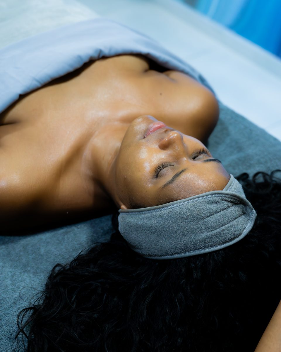 Guest lying back in a headband after a facial, skin left with a natural sheen.
