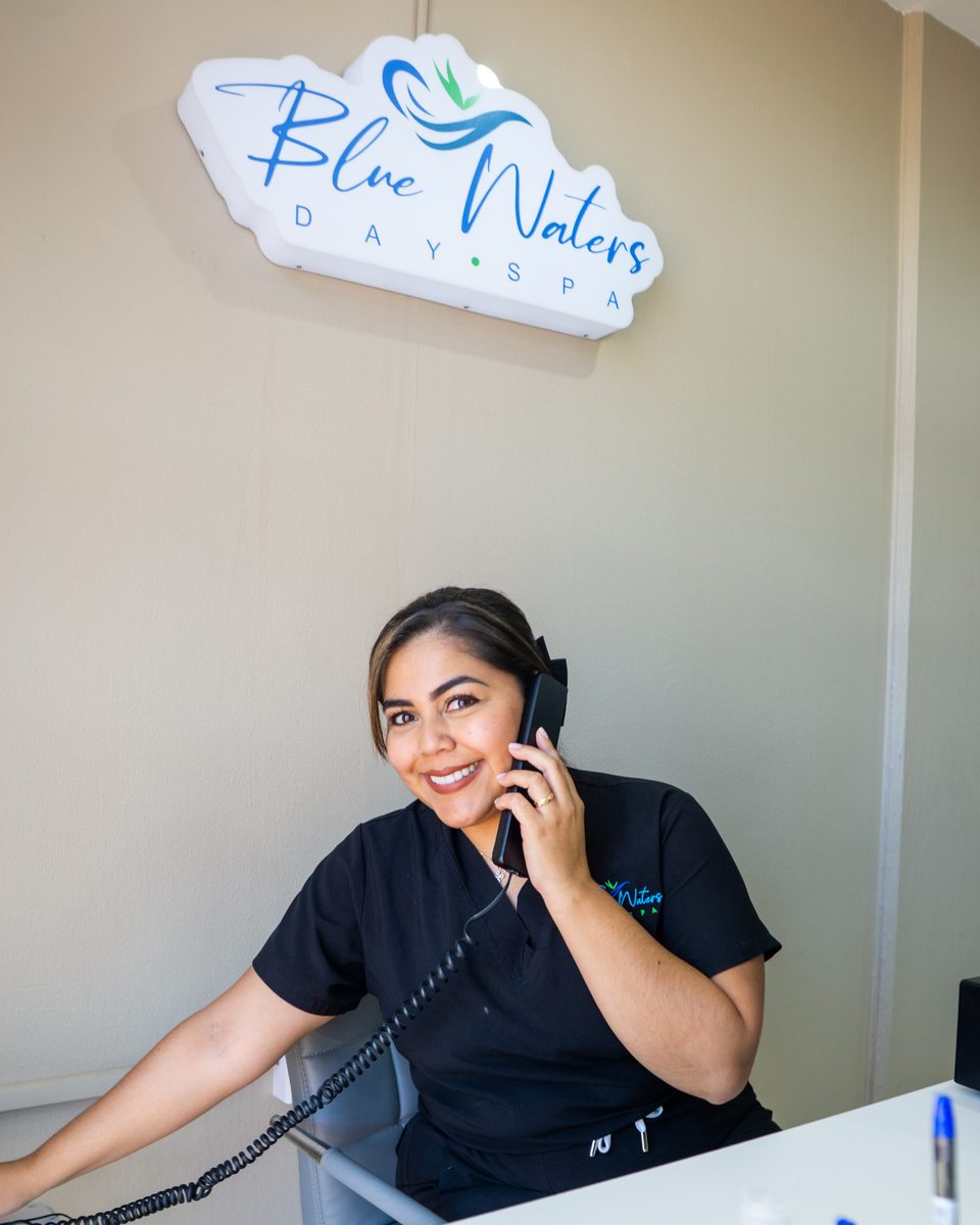 Receptionist taking a booking by phone beneath the illuminated Blue Waters Day Spa sign.