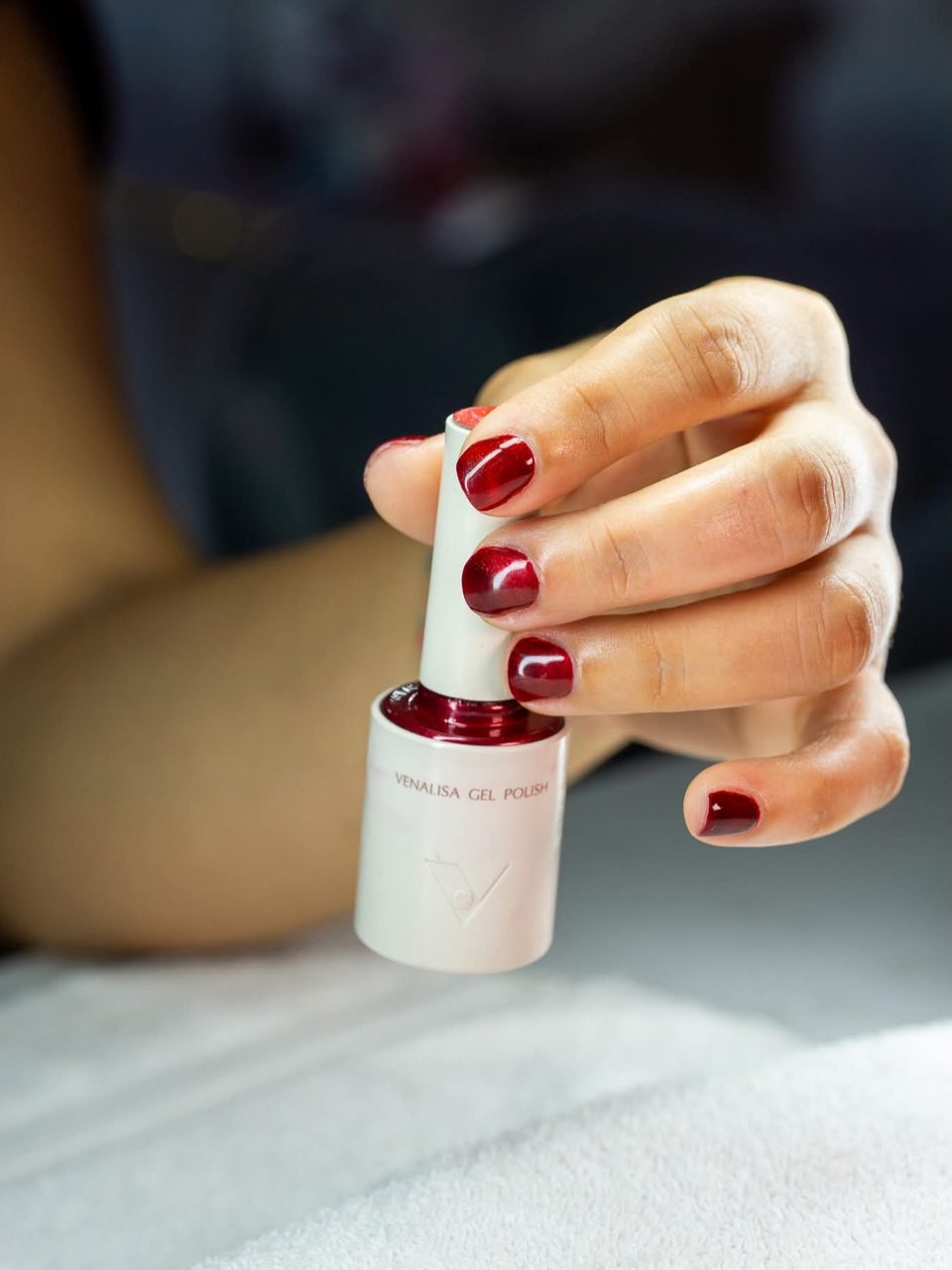Freshly painted red nails holding a bottle of matching gel polish.