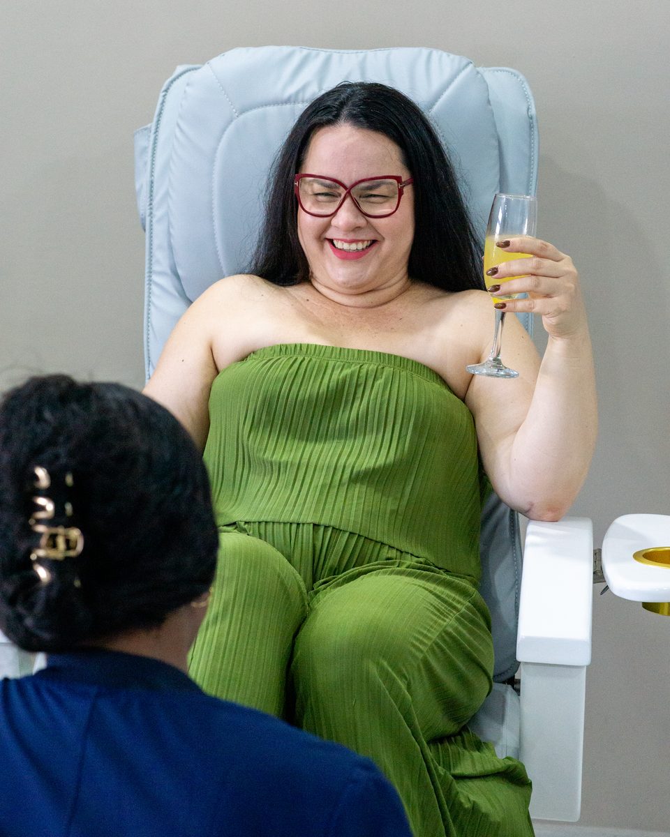 Guest laughing in a spa chair with a drink, wrapped in a green towel.