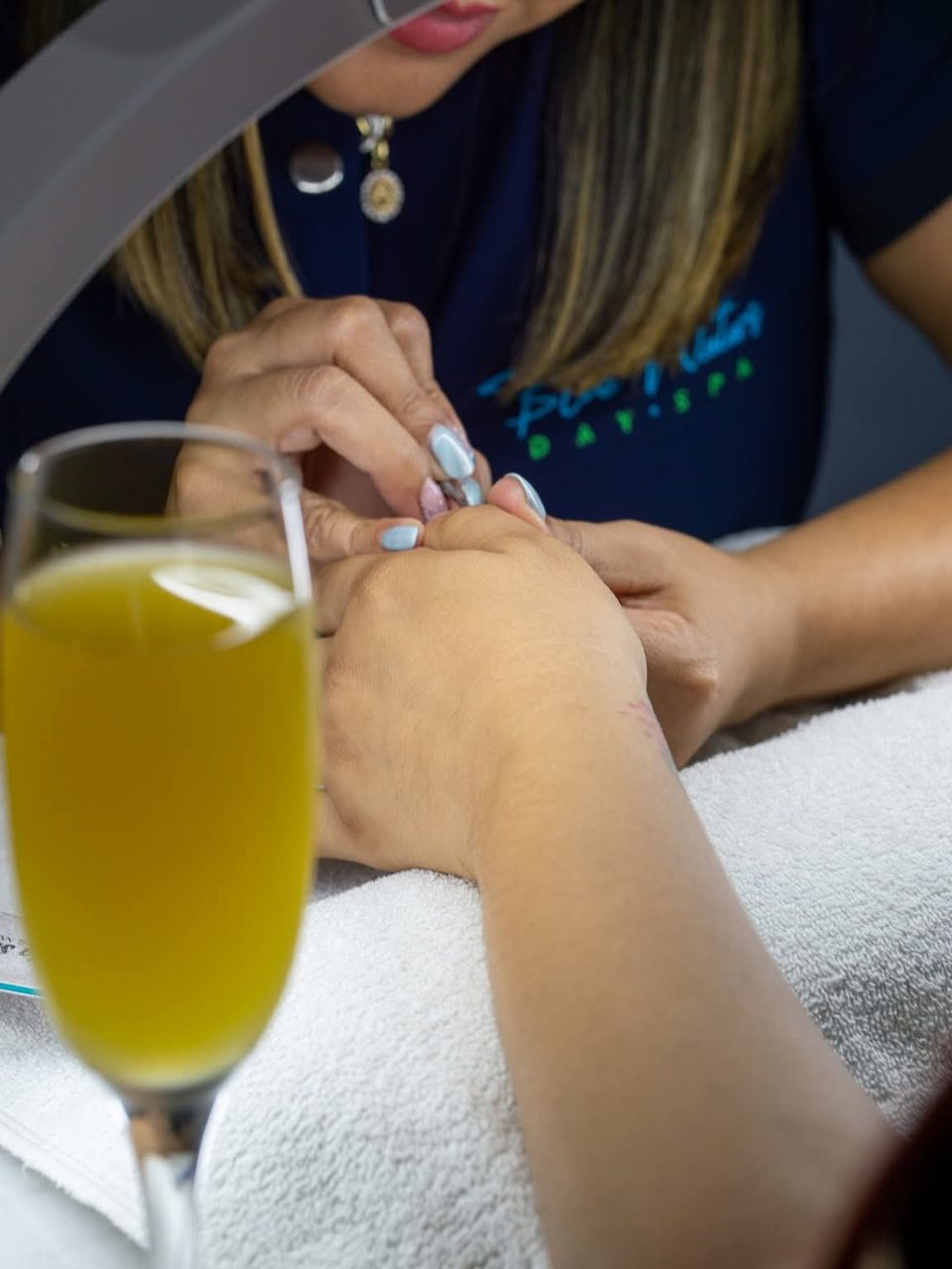 Manicure in progress beside a glass of sparkling welcome drink.