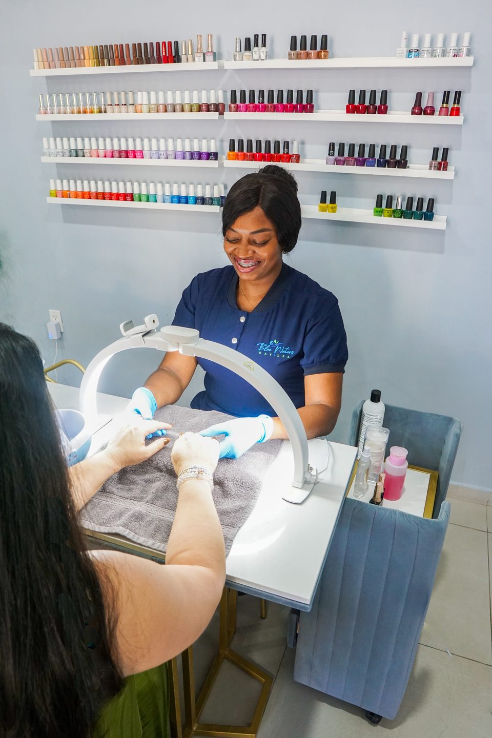 Manicure underway at a station backed by a full wall of polish colors.