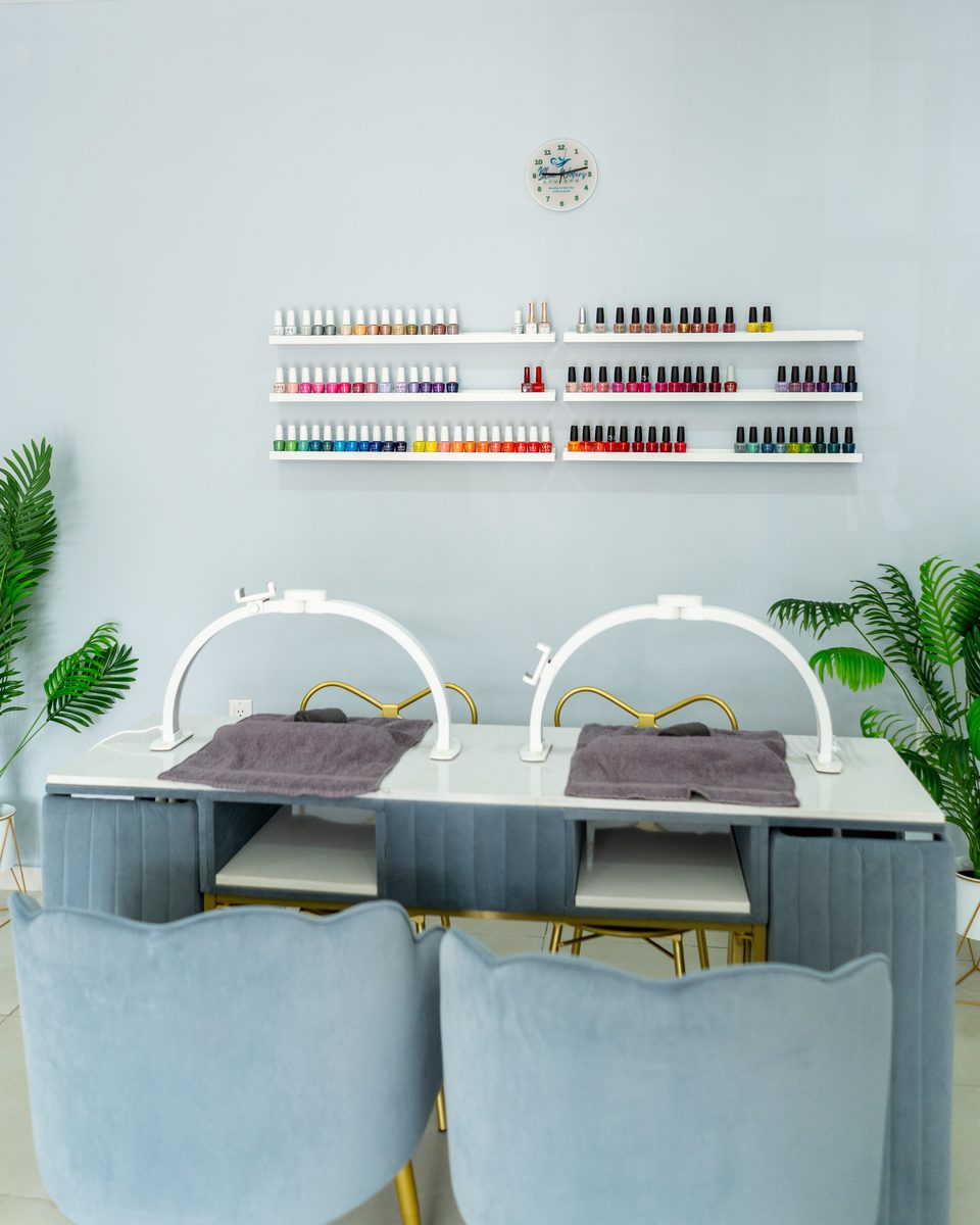 Manicure table set for two, with a full wall rack of nail polish colors behind it.