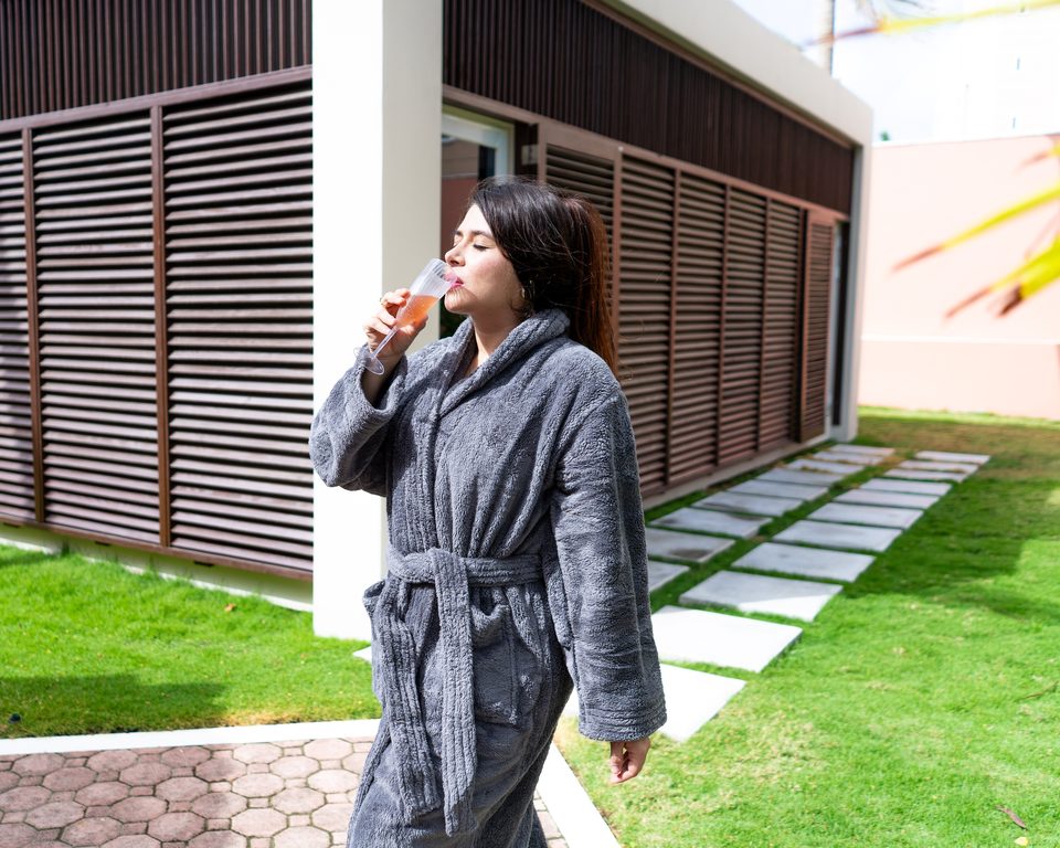 Guest in a plush gray robe sipping a glass of sparkling wine on the stepping-stone path through the garden.
