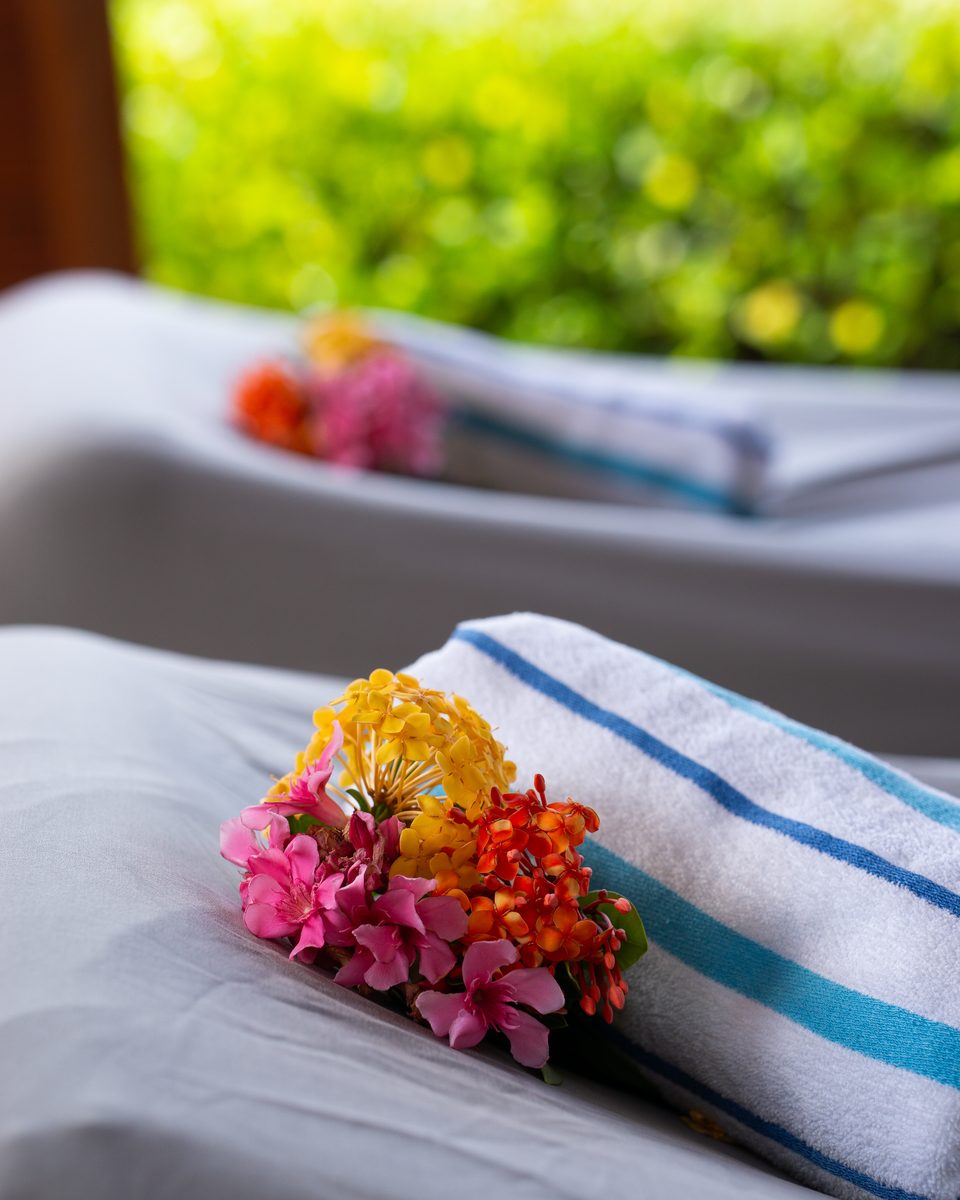 Folded towels topped with fresh tropical flowers on a treatment bed.